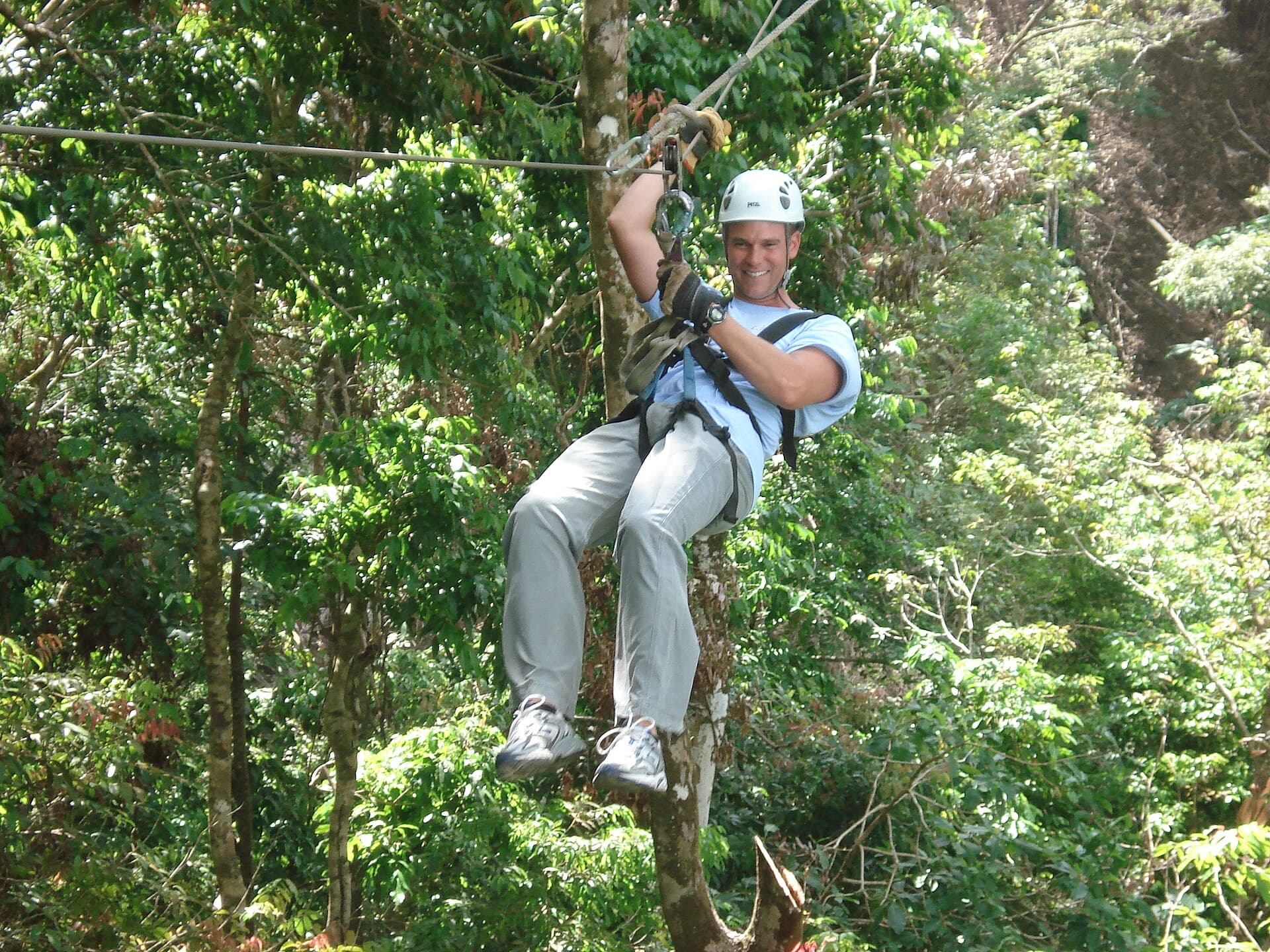 A smiling man ziplining through rainforest canopy in Costa Rica