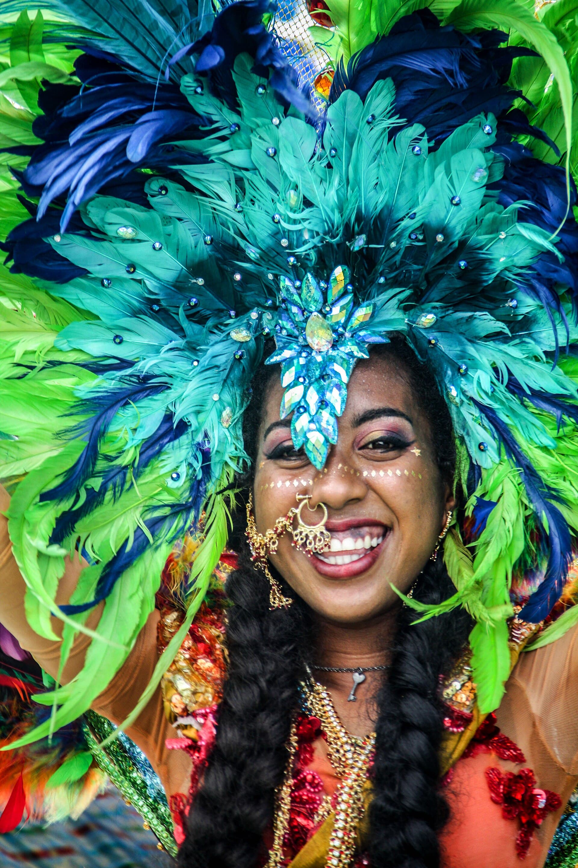 A smiling Indo-Trinidadian woman in festive traditional jewelry and a feathered headpiece